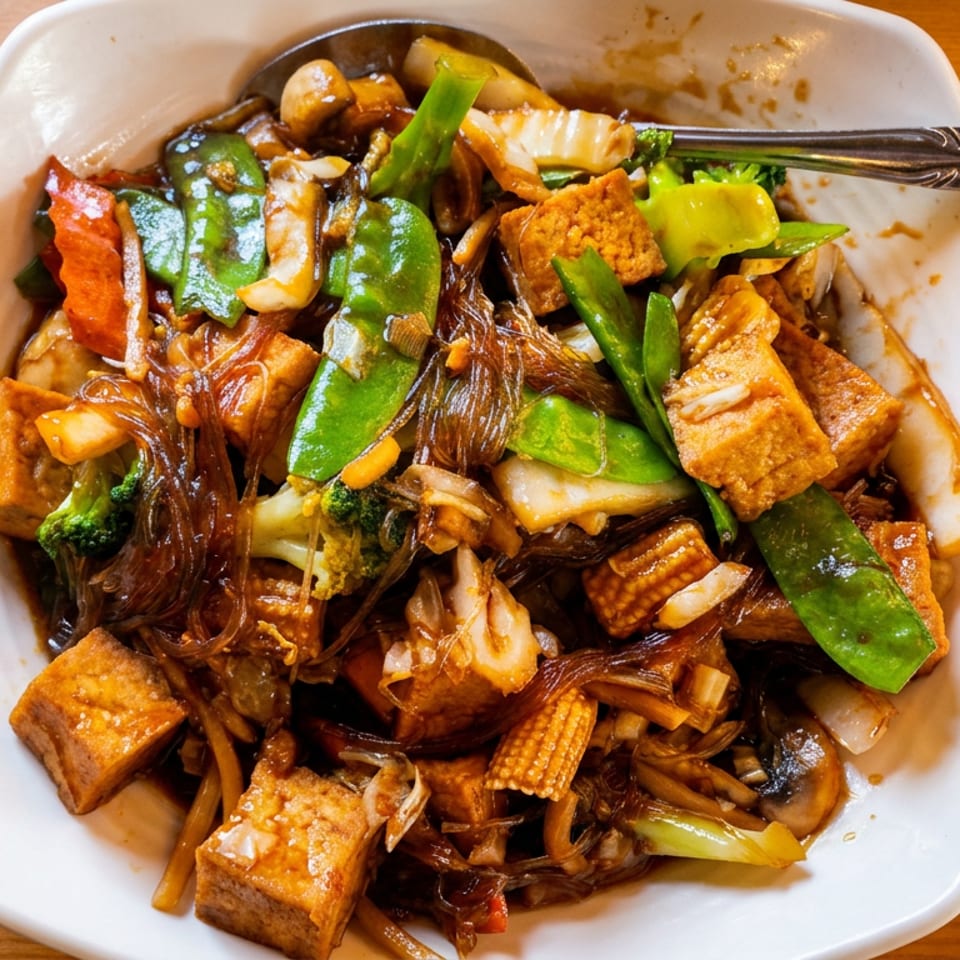 A white bowl filled with stir-fried glass noodles, tofu, and mixed vegetables on a wooden table.