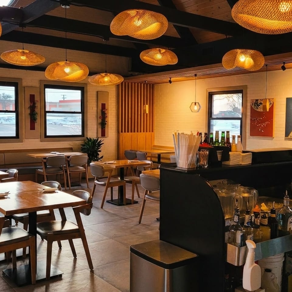 Modern restaurant interior with wooden tables, wicker pendant lights, and a bar area.