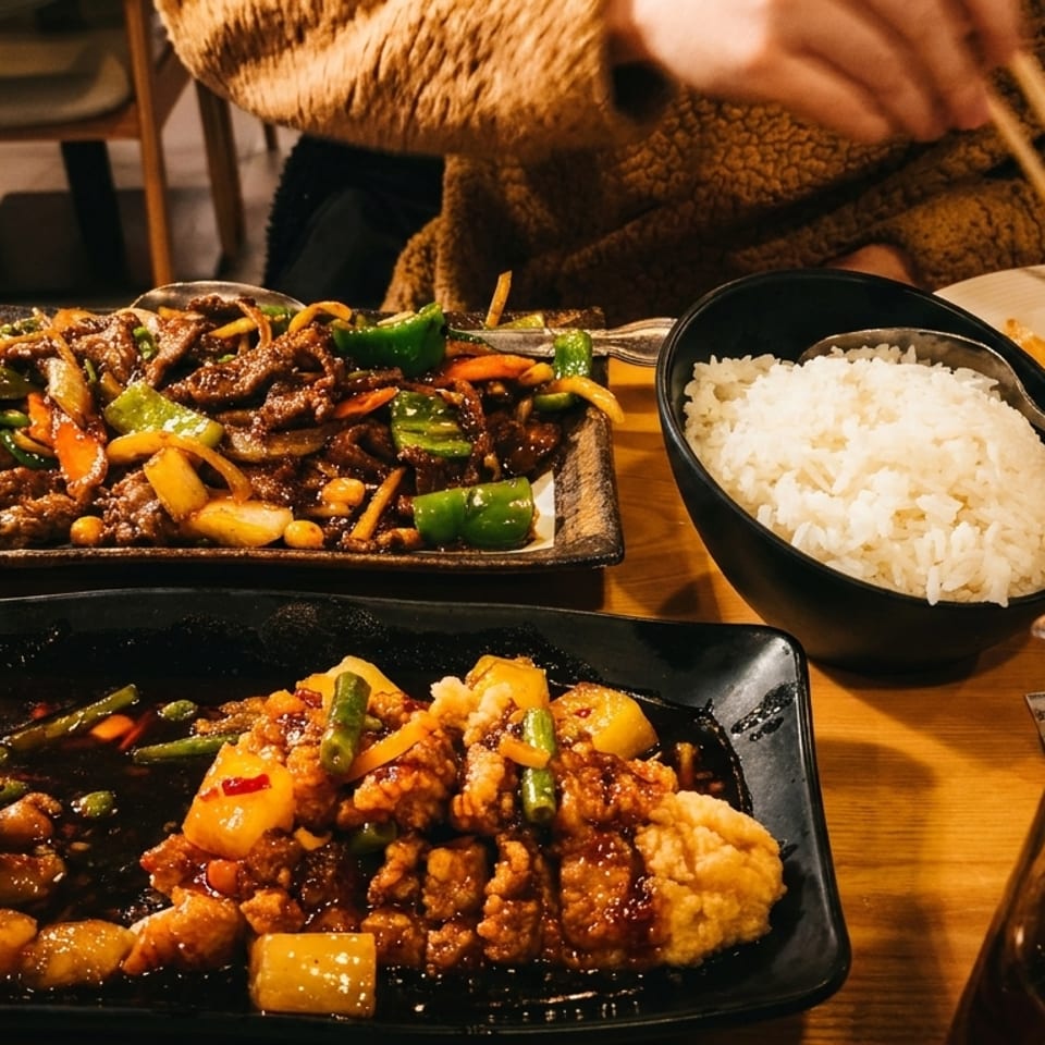 A table laden with various Asian dishes, including stir-fry, rice, and a person eating with chopsticks.