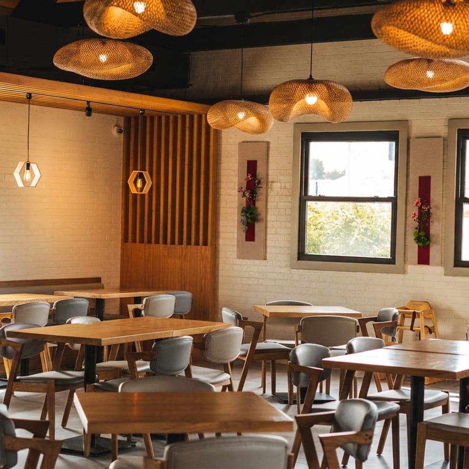 A modern restaurant interior with wooden tables, gray chairs, large windows, and woven pendant lights.